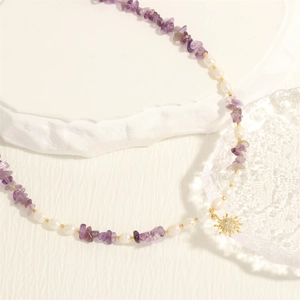 Detail of freshwater pearl necklace with purple stones and a golden sun charm