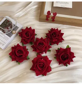 Detailed view of six red velvet rose hair clips on white satin fabric background