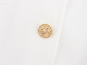 Close-up of a gold textured button with woven pattern on a white corduroy dress