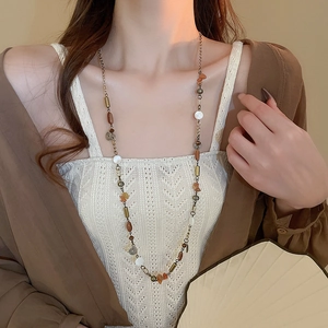 Dettaglio di una lunga collana vintage con pietre marroni e perline bianche tonde