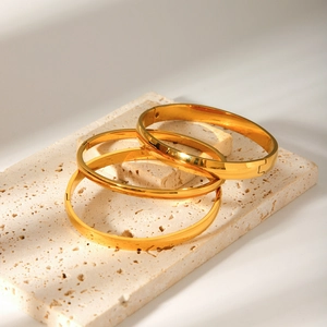 Three-piece gold plated stainless steel bangles set with polished finish on stone tray