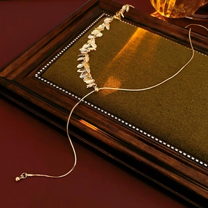 Close-up of golden leaf tassel necklace on green velvet display board with snake chain