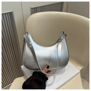 Detailed view of silver bow-knot handbag with adjustable strap on a book and beige chair