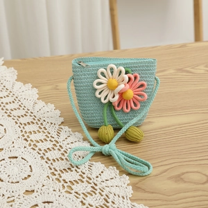 Detail of mint green woven crossbody bag with large 3D crochet flowers on a wood surface