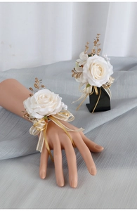 Dettaglio di fiore all'occhiello e polsino con rose bianche, foglie d'oro e nastri