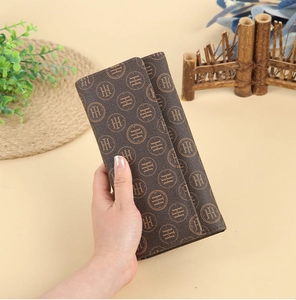 Detail of hand holding dark brown long wallet with vintage logo pattern and leather texture