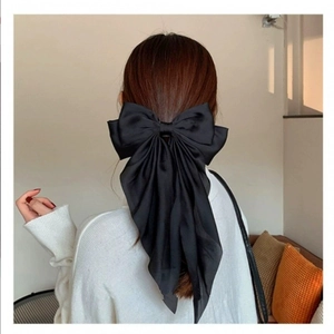 Detail of a large black satin bow hair clip with long ribbons worn on a model's hair
