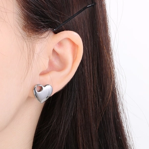 Close-up of a silver heart-shaped stud earring worn by a model in a minimalist style