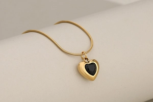 Detailed macro shot of a gold-plated snake chain necklace with a black heart crystal