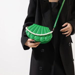 Green shell-shaped crossbody bag with pearl chain detail worn on a black blazer