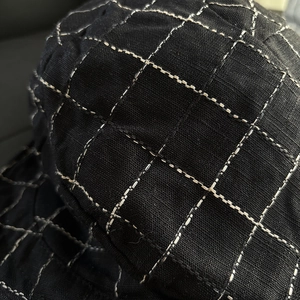 Detailed close-up showing white stitching on black checkered linen fabric of the beret cap
