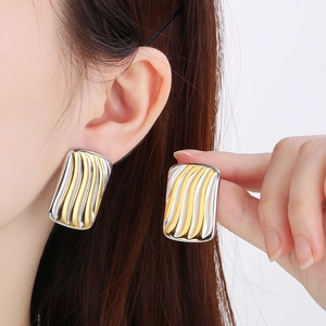 Detail of two-tone gold and silver wave pattern rectangular stud earrings on model