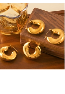 Dettaglio di orecchini a cerchio dorati spessi a forma di C su un vassoio di legno vintage