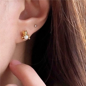 Close-up of golden bear earring with white pearl worn on ear for detailed view