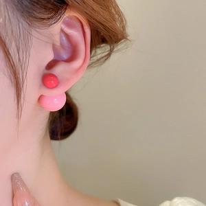 Detail of pink and red double-sided ball earrings on ear with glossy resin finish