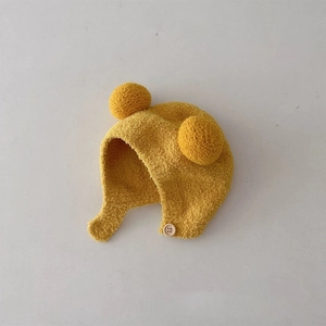 Detail of yellow knitted baby hat with soft pom-poms and functional side button closure