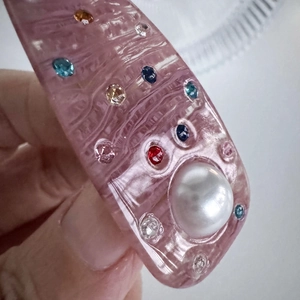 Pink acetate hair clip with colorful crystals and pearl detail held by hand