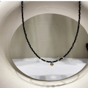 Vue détaillée d'un collier de perles en cristal noir avec un pendentif boule dorée minimaliste.