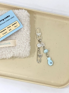 Detailed view of handmade light blue fish phone charm with star beads and shell on a tray