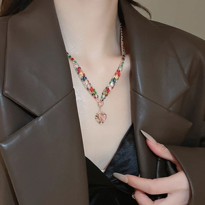 Detail of V-shaped gold necklace with colorful crystals and pink heart pendant on model