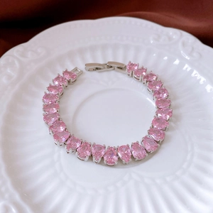 Macro shot of pink pear-cut zircon bracelet with silver-tone folding clasp on silk