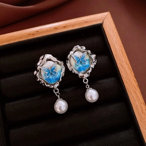 Macro detail of butterfly earrings featuring blue enamel sky and white pearl drops