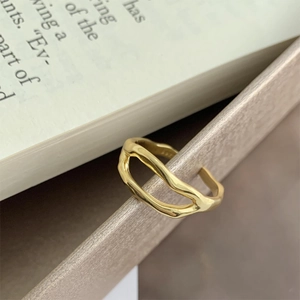 Macro detail of a 925 sterling silver golden irregular wavy open ring on a textured stand