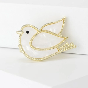Detailed close-up of a golden dove brooch with white pearlescent inlay on white stands