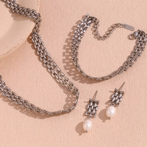 Detailed set of silver steel woven necklace, bracelet and pearl drop earrings on pink background