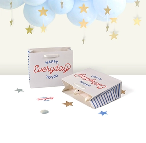 Detail of square white paper gift bag with satin handles and colorful happy text