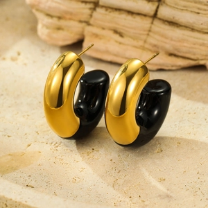 Macro view of C-shaped 18k gold and black enamel earrings on stone texture