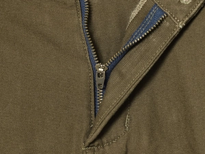Detailed macro view of bronze metal zipper and stitching on olive green cargo pants