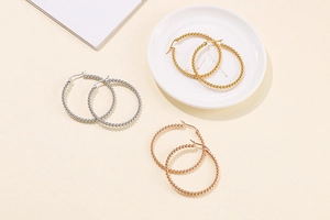 Detailed close-up of three pairs of wide-beaded hoop earrings in gold, silver, and rose gold