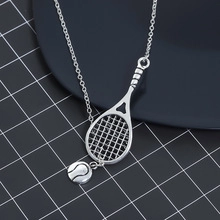 Close-up of a silver-toned tennis racket and ball pendant necklace on a textured black mat
