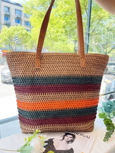 Detail of colorful raffia woven beach tote with striped pattern and brown leather handles