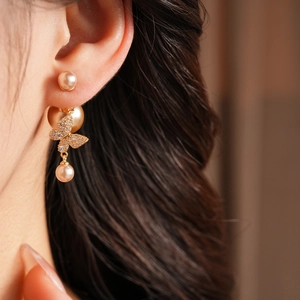 Detail view of vintage gold plated butterfly pearl earring worn by model in soft lighting