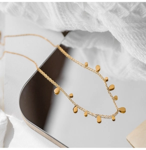 Detailed view of a gold titanium teardrop pendant necklace on a reflective surface