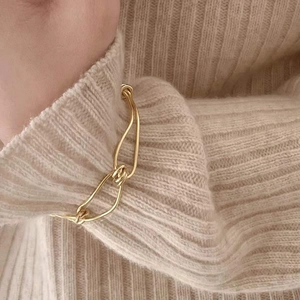 Close-up of gold knotted chain bracelet styled on wrist with a beige knit sweater