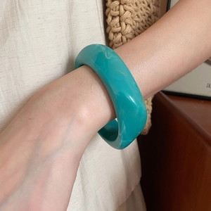 Detailed close-up of a wide turquoise resin bangle with marble texture on woman's wrist