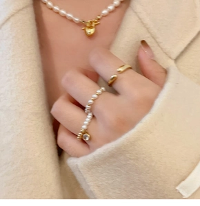 Détail du collier coeur doré et bagues perles portés sur un manteau en laine beige
