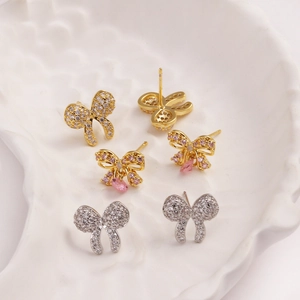 Sparkly bow zircon stud earrings set in gold and silver finishes on shell tray