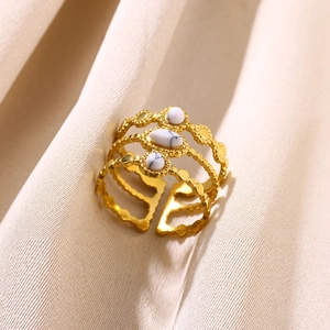 Detailed close-up of a three-layered gold ring with white oval stones on beige fabric
