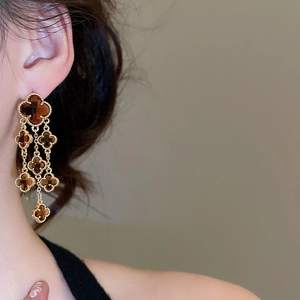 Detail view of long golden fringe earrings with amber clover crystals on a model