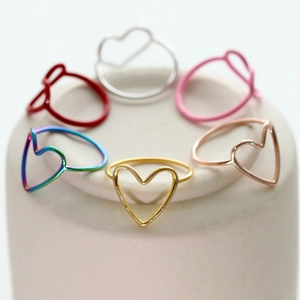 Minimalist heart-shaped open rings in six metallic colors on a ceramic pedestal