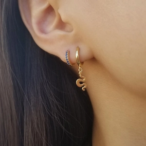 Detail of gold snake charm hoop earring and blue pavé zircon studs on a model ear
