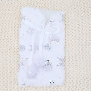 Detailed view of white faux fur wine bottle cover featuring silver snowflakes and pom-poms