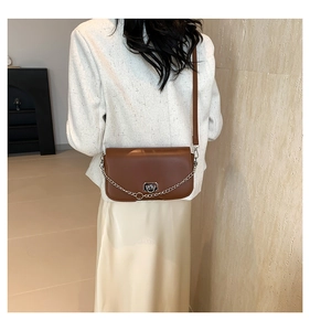 Détail du sac à bandoulière en cuir marron avec chaîne argentée et fermoir rotatif rond