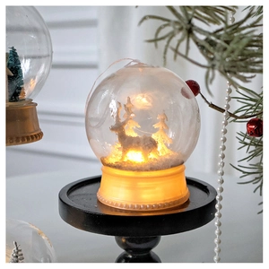 Close-up of reindeer and Christmas tree inside a warm glowing glass globe ornament