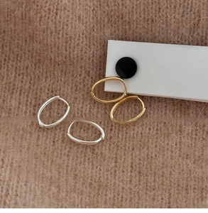 Dettaglio di orecchini a cerchio ovali in oro e argento su sfondo in maglia calda