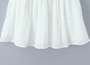 Detailed close-up of white dress fabric with floral embroidery and hollow-out lace design